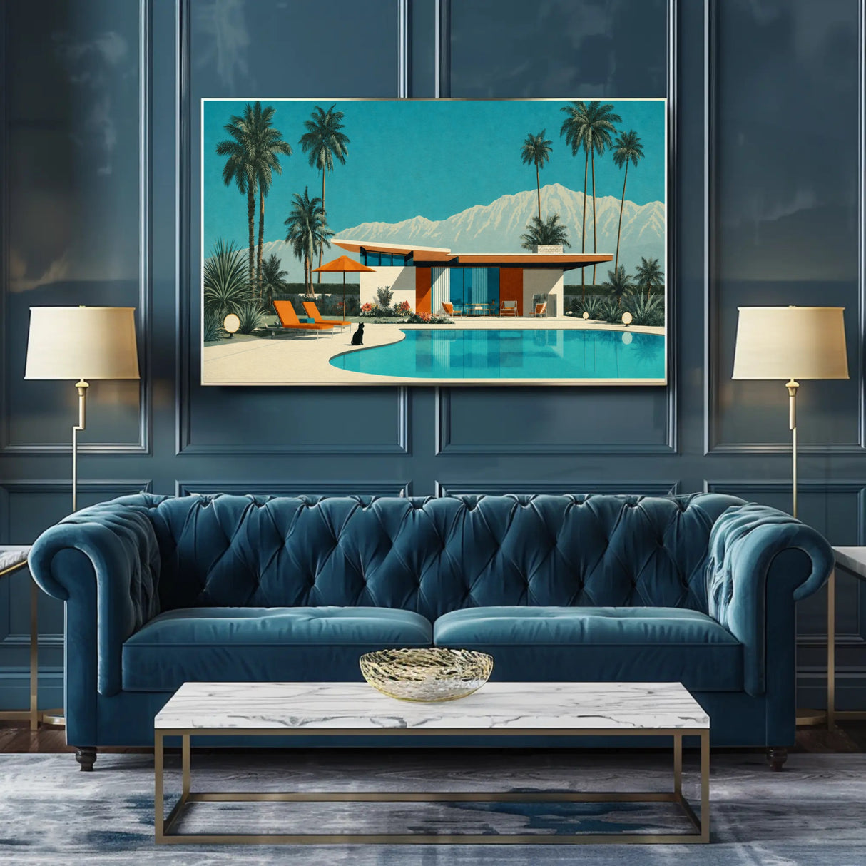 A framed art print depicting a retro mid-century modern poolside house with palm trees and mountains, displayed on a dark blue paneled wall above a matching blue tufted sofa in a styled living room.