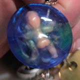 Hand holding a blue cute/creepy keychain with a in a blue green half sphere, with keys in the background.