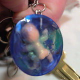 Hand holding a blue circular reein cute creepy baby with bum showing with a keychain attached