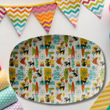 An oval decorative serving platter with a colorful retro 1960s pattern of black cats, surfboards, candles, and geometric shapes on a cream background, displayed on a white surface with bunting and patterned paper props.
