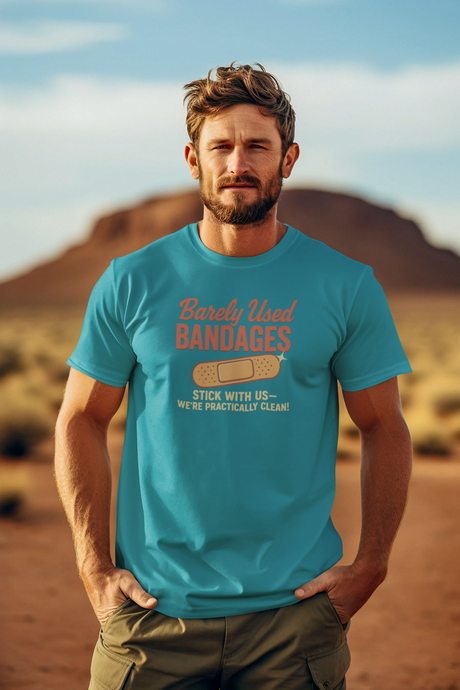 A man standing in a desert setting, wearing a blue T-shirt with a retro graphic that says 'Barely Used Bandages'.