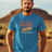 A man standing in a desert setting, wearing a blue T-shirt with a retro graphic that says 'Barely Used Bandages'.