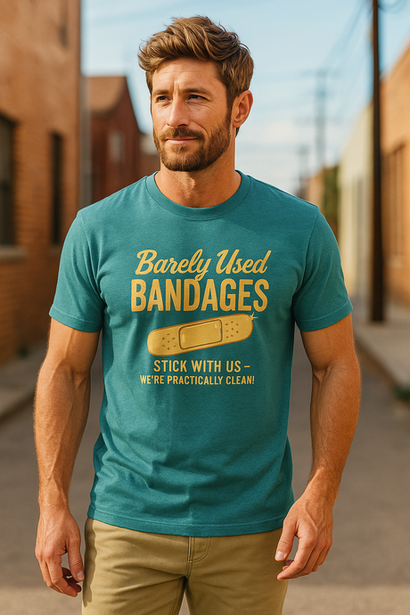 A man standing in a desert setting, wearing a blue T-shirt with a retro graphic that says 'Barely Used Bandages'.