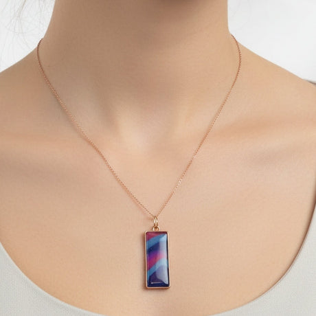 Woman wearing a necklace with a colorful pendant on a plain background