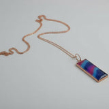 Rectangular pendant with a colorful design on a chain against a light gray background