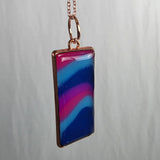 Colorful rectangular pendant on a chain against a gray background