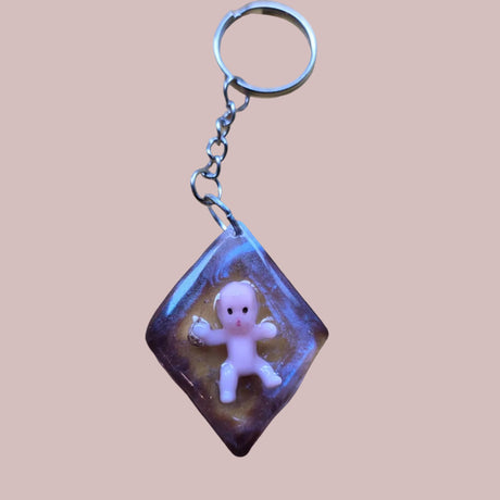 Keychain with a small figurine inside a purple frame on a brown surface