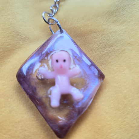 Small figurine inside a diamond -square clear/purple pendant on a yellow fabric background